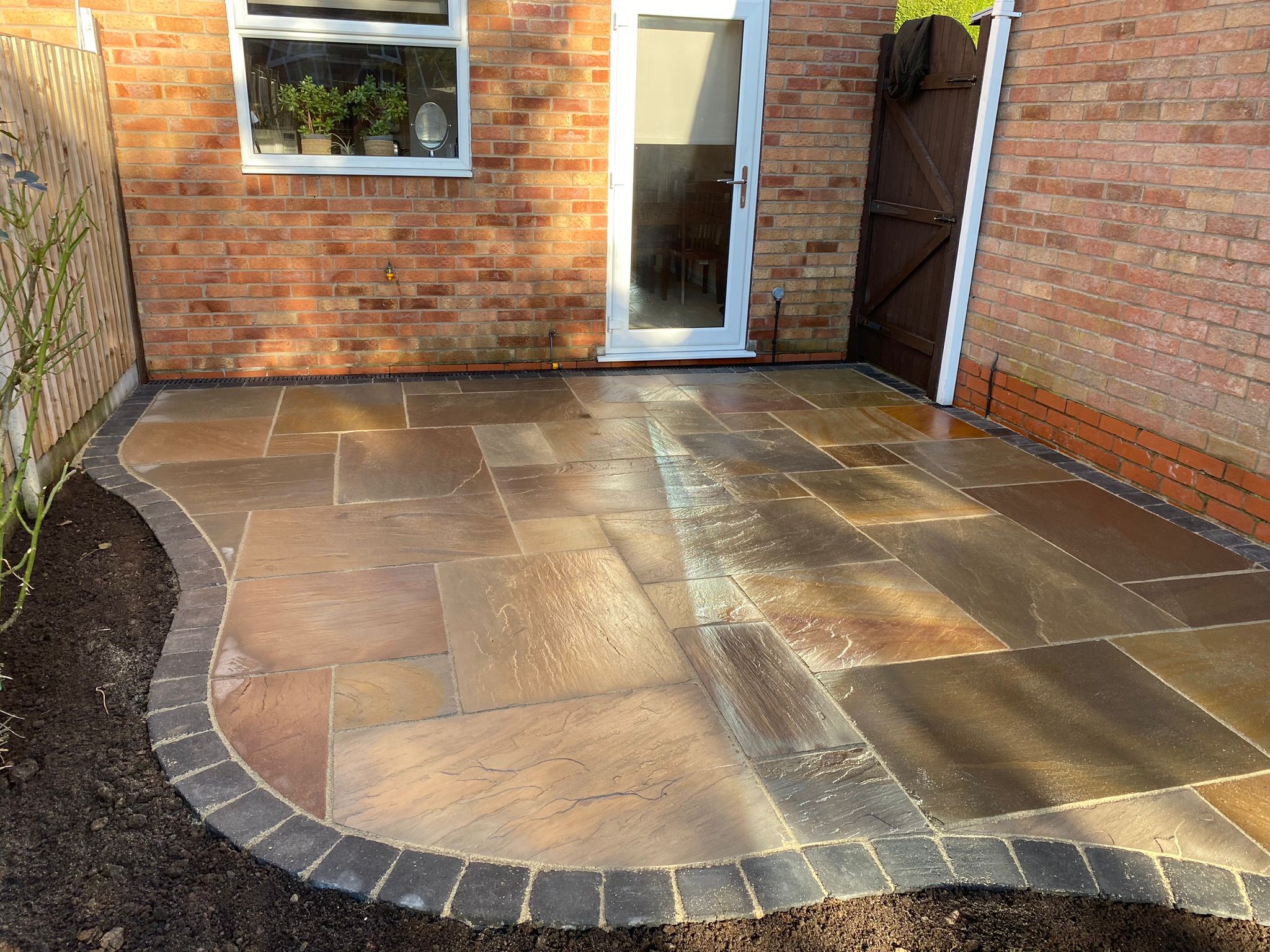Curved Indian sandstone patio with a charcoal sett border